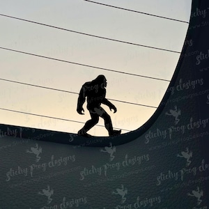 May include: Silhouette of a Bigfoot figure walking across a curved surface, set against a gradient sky. The image is a dark silhouette, with the creature's form clearly defined. The background features horizontal lines and a textured surface.