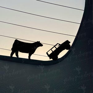 May include: Black silhouette decal featuring a cow and a truck. The cow stands on the left, while the truck is angled upwards on the right. The background shows a gradient of light colors.
