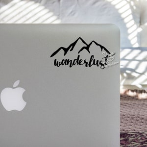 May include: A black and white sticker with a mountain range silhouette and the word "wanderlust" in cursive script.