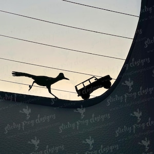 May include: A black silhouette of a roadrunner running away from a black silhouette of a car on a car window. The car is driving up the window and the roadrunner is running to the left. The text "Sticky Frog Designs" is visible in the image.