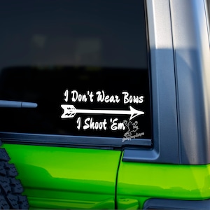 May include: White vinyl decal with an arrow pointing to the right. The text reads "I Don't Wear Bows I Shoot 'Em".