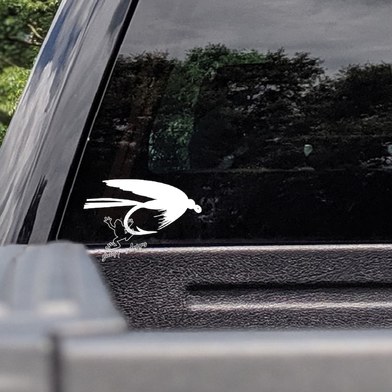 May include: White silhouette of a fly fishing lure with a frog on a black car window.