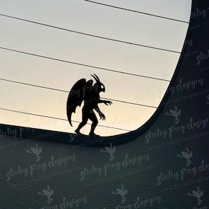 May include: A black silhouette of a gargoyle with large wings, horns, and clawed hands and feet. The gargoyle is standing on a curved surface against a backdrop of a gradient sky. The image has a sticker design.