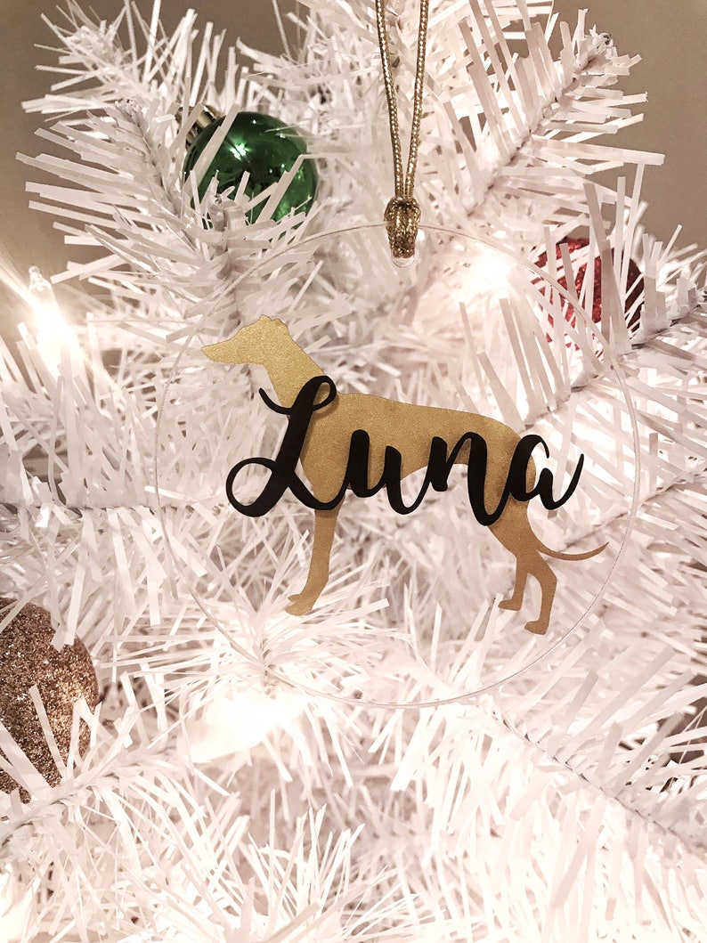 May include: A clear round Christmas ornament with a gold silhouette of a dog and the name "Luna" written in black cursive.
