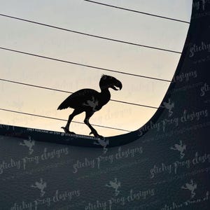 May include: A black silhouette of a prehistoric bird with a large beak and long legs, walking on a curved surface. The background features horizontal lines and a gradient sky. Text at the bottom reads "ONLY PURCHASE on ETSY @ STICKYFROGDESIGNS.COM".