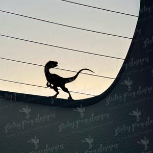 May include: A black silhouette of a raptor dinosaur is set against a backdrop of horizontal lines and a gradient sky. The dinosaur is in a walking pose, with its tail extended. The image has a minimalist design.