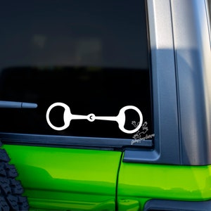 May include: White vinyl sticker of a horse bit on a green car window.