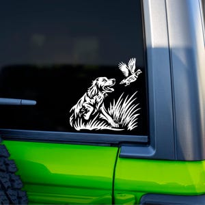 May include: White vinyl decal featuring a dog sitting in tall grass, looking up at a flying bird. The decal is applied to a black window, with a green vehicle door frame visible.