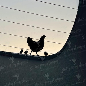 May include: A black silhouette of a hen with three chicks. The hen is walking, and the chicks are standing nearby. The background is a gradient of light and dark, with horizontal lines. Text at the bottom reads "ONLY PURCHASE ON ETSY @ STICKYFROGDESIGNS.COM".