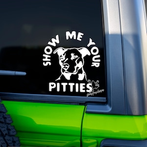 May include: White vinyl decal with a silhouette of a Pit Bull dog and the text "Show Me Your Pitties" in a circle. The decal is on a green car window.