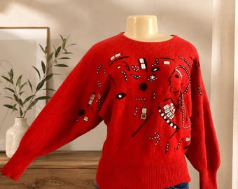 May include: A vibrant red long-sleeve sweater featuring a crew neckline and ribbed cuffs and hem. The front is decorated with an abstract embroidered design in white and black thread, accented by small clear rectangular and round embellishments.