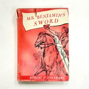 Peut inclure: Couverture de livre vintage pour "Mr. Benjamin's Sword" de Robert D. Abrahams. Le fond est rouge, avec une bannière blanche en haut affichant le titre. Une illustration représente un homme à cheval, levant son chapeau. Le titre et l'auteur du livre sont visibles.
