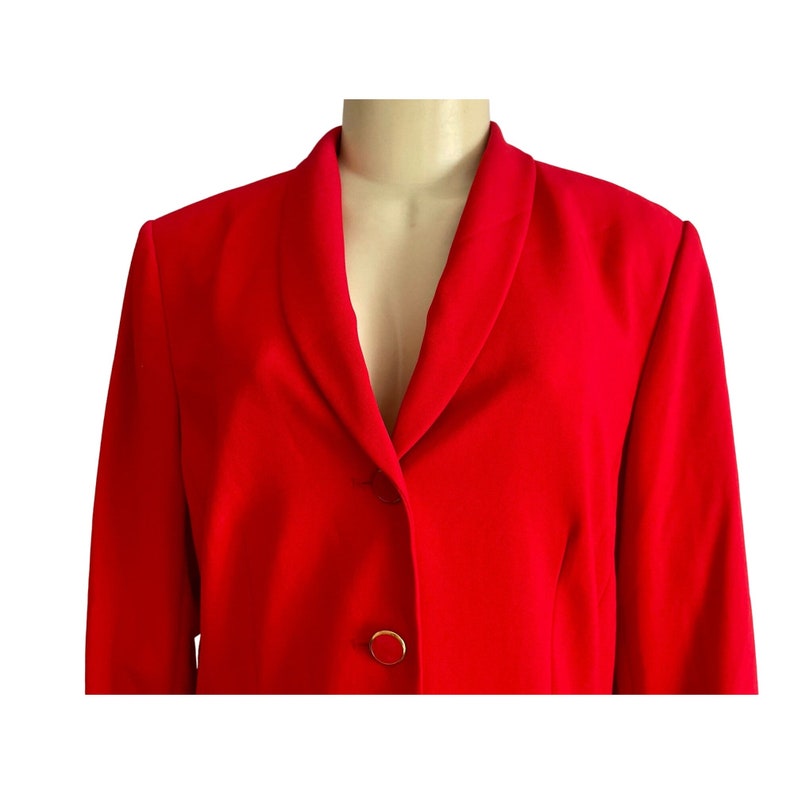 May include: A vibrant red blazer featuring a shawl collar and a front closure with two circular buttons. The jacket has long sleeves and a structured fit, showcasing a solid, bold red color throughout the entire garment design.