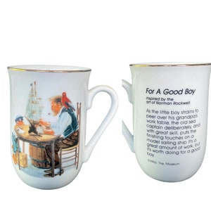May include: A white ceramic mug with a gold rim featuring a Norman Rockwell illustration of a sea captain and a child building a model ship. The reverse side displays the text: For A Good Boy, inspired by the art of Norman Rockwell, 1986 The Museum.