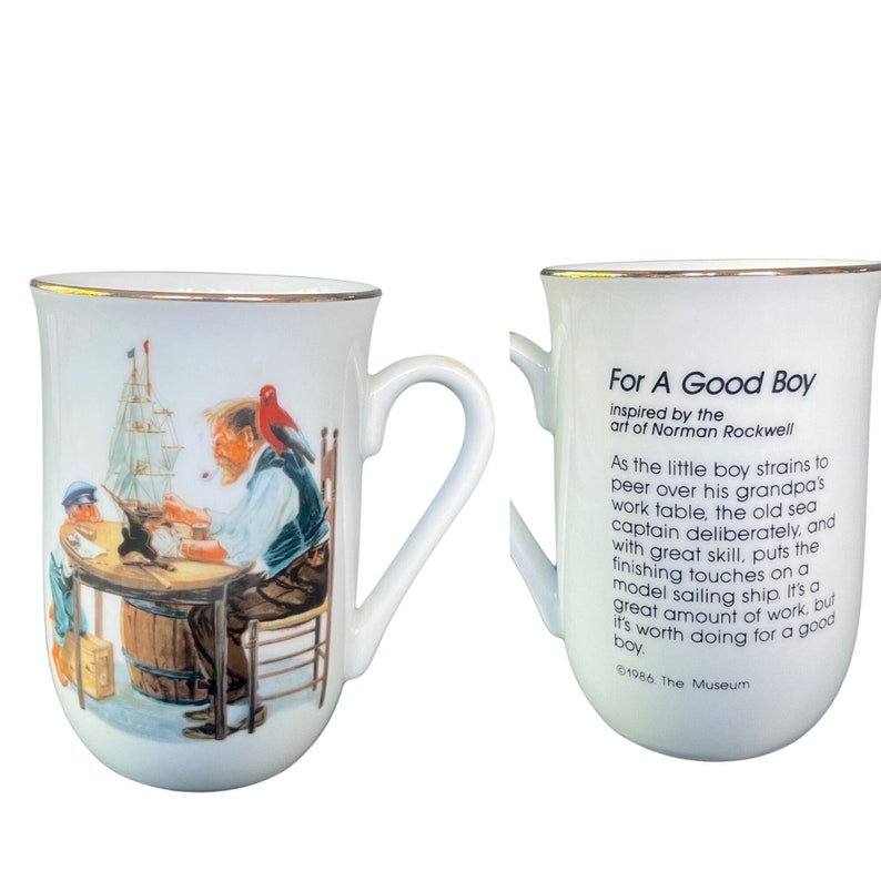 May include: A white ceramic mug with a gold rim featuring a Norman Rockwell illustration of a sea captain and a child building a model ship. The reverse side displays the text: For A Good Boy, inspired by the art of Norman Rockwell, 1986 The Museum.