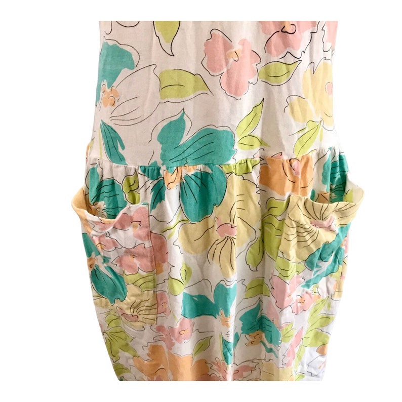 May include: A sleeveless dress with a floral pattern in pastel colors. The dress features large, stylized flowers in shades of pink, yellow, and teal, outlined in black. It has two large pockets and a gathered waistline, creating a relaxed, summery look.
