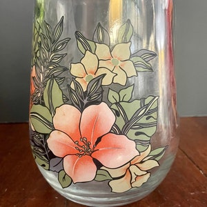 Puede incluir: Una jarra de vidrio transparente con un dise&ntilde;o floral. El dise&ntilde;o presenta flores rosas, amarillas y verdes con contornos negros.