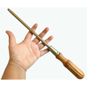 Puede incluir: Un destornillador vintage con mango de madera y vástago de metal. El mango es de color marrón claro y tiene una superficie texturizada. El vástago de metal es plateado y tiene una punta ligeramente curvada.