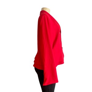 May include: A vibrant red blazer featuring a notched lapel, long sleeves, and a double-breasted front closure with visible buttons. The garment is displayed on a mannequin, showcasing a structured silhouette with a straight hemline and clean lines.