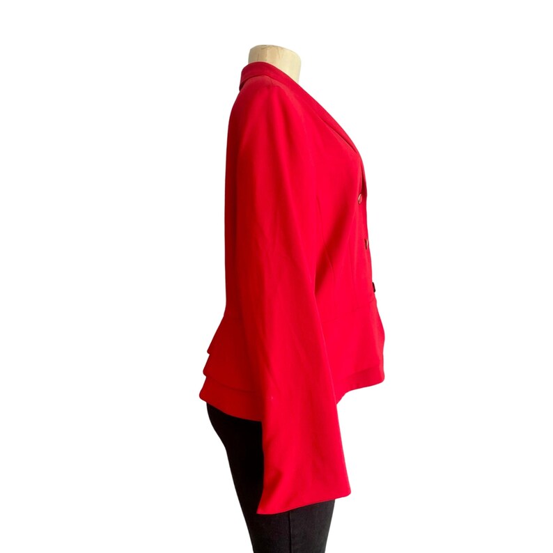 May include: A vibrant red blazer featuring a notched lapel, long sleeves, and a double-breasted front closure with visible buttons. The garment is displayed on a mannequin, showcasing a structured silhouette with a straight hemline and clean lines.