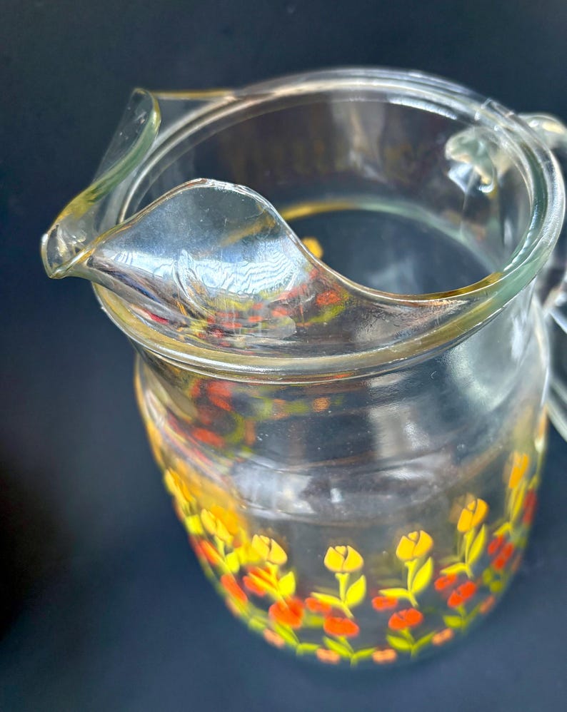 May include: A clear glass pitcher with a floral design. The pitcher has a yellow, orange, and red floral pattern around the bottom.