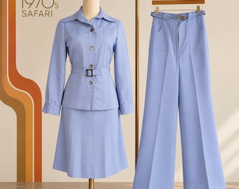 May include: A light blue two-piece outfit consisting of a long-sleeved button-down shirt with a belt and a matching skirt, displayed on a mannequin, alongside a pair of matching wide-leg trousers hanging on a rack. The text 1970s SAFARI is visible.