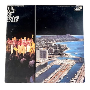 May include: Vintage vinyl record album cover for "The Best of Hawaii Calls." The album cover features a black background with the title and a photo of a band in red floral shirts. The right side shows a scenic view of a city, ocean, and mountain.