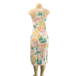 May include: A sleeveless floral print dress with a white racerback design. The dress features a pattern of large flowers in pastel colors, including pink, yellow, and teal, set against a white background. The dress is knee-length and has a gathered waist.