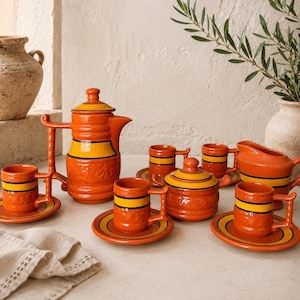 May include: A ceramic tea set featuring a tall teapot, a lidded sugar bowl, a creamer, and three cups with matching saucers. Each piece is finished in a vibrant orange glaze with a prominent horizontal yellow band and black accent stripes.