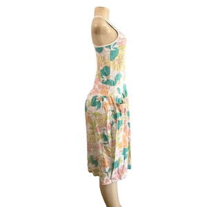 May include: A white sundress with a floral pattern in shades of pink, yellow, green, and blue. The dress has a scoop neck, a fitted bodice, and a knee-length skirt with pockets. The dress is displayed on a mannequin.