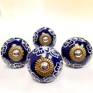 May include: Four navy blue ceramic cabinet knobs with white floral designs and gold and silver center accents. These decorative knobs are a stylish addition to any furniture piece.