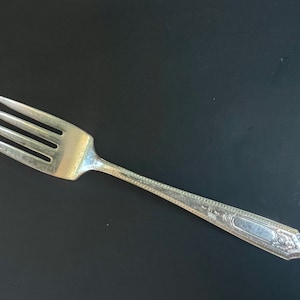 May include: A silver fork with a decorative handle. The fork has four tines and a slightly curved handle.