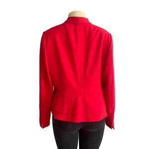 May include: A vibrant red blazer featuring a structured collar, long sleeves, and a double-layered peplum hem. The garment is displayed on a mannequin torso, showcasing a solid color finish and a tailored fit that flares slightly at the waistline.