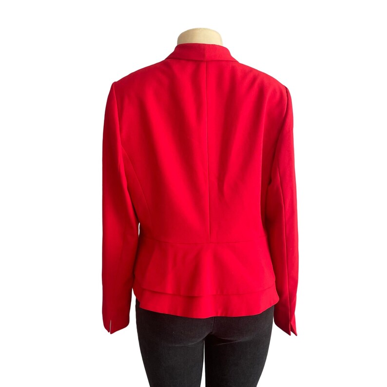 May include: A vibrant red blazer featuring a structured collar, long sleeves, and a double-layered peplum hem. The garment is displayed on a mannequin torso, showcasing a solid color finish and a tailored fit that flares slightly at the waistline.