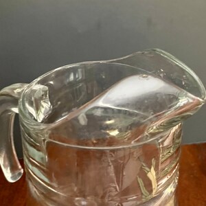 Puede incluir: Una jarra de vidrio transparente con una boca ancha y un asa. La jarra tiene una superficie texturizada y est&aacute; dise&ntilde;ada para servir bebidas.