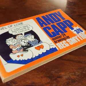 May include: A vintage comic book titled "Andy Capp" by Reg Smythe. The cover is orange and blue, featuring cartoon illustrations and the text "Tunnel of Love." The comic book is number 24 and priced at 3/6.