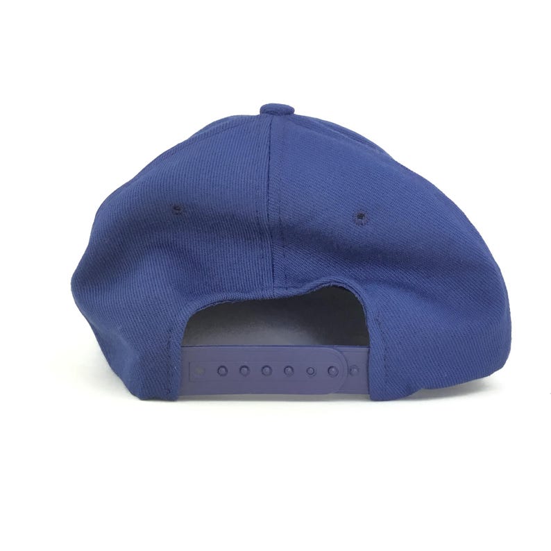 May include: A solid blue baseball cap with a curved brim and adjustable snapback closure. The cap is made of a textured fabric and features a button on top. The back of the cap is visible, showing the adjustable strap.