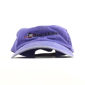 Puede incluir: Una gorra de béisbol morada con visera curva y un logotipo bordado en la parte delantera. El logotipo presenta un pequeño gráfico de un globo terráqueo rodeado por una fina línea roja, seguido del texto negro Blackbaud.
