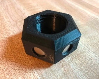 Può includere: Un oggetto esagonale nero stampato in 3D con un centro vuoto e due aperture circolari su ogni lato. L'oggetto ha una superficie testurizzata.