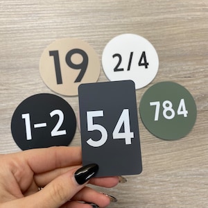 May include: Five round and rectangular signs with numbers on them. The signs are beige, white, black, green, and grey. The numbers on the signs are 19, 2/4, 1-2, 784, and 54.