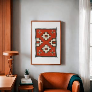 May include: A framed print of a Native American rug with a geometric pattern in red, white, and black. The rug is in a wooden frame and is hanging on a light gray wall.