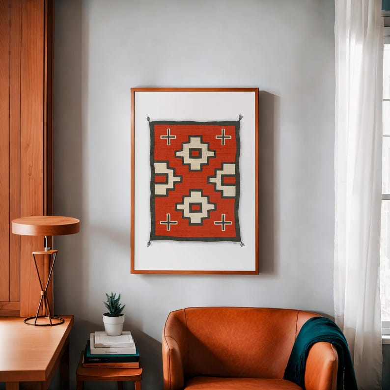 May include: A framed print of a Native American rug with a geometric pattern in red, white, and black. The rug is in a wooden frame and is hanging on a light gray wall.