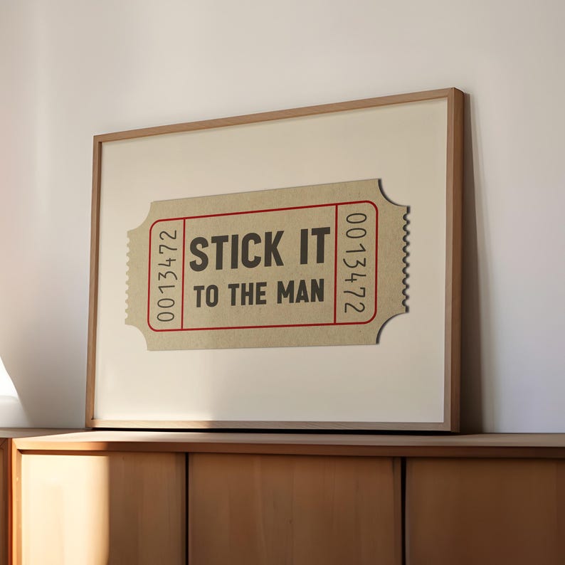 May include: A framed print of a brown ticket with the text "STICK IT TO THE MAN" in black letters and the number "0013472" on either side of the ticket.