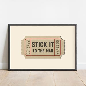 May include: A framed print of a vintage ticket with the text "STICK IT TO THE MAN" printed on it. The ticket has the numbers 0013472 printed on the right side and 0013472 printed on the left side.