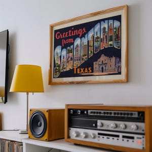 May include: A framed print with the words "Greetings from San Antonio Texas" in a vintage postcard style. The print is above a yellow lamp and stereo equipment.