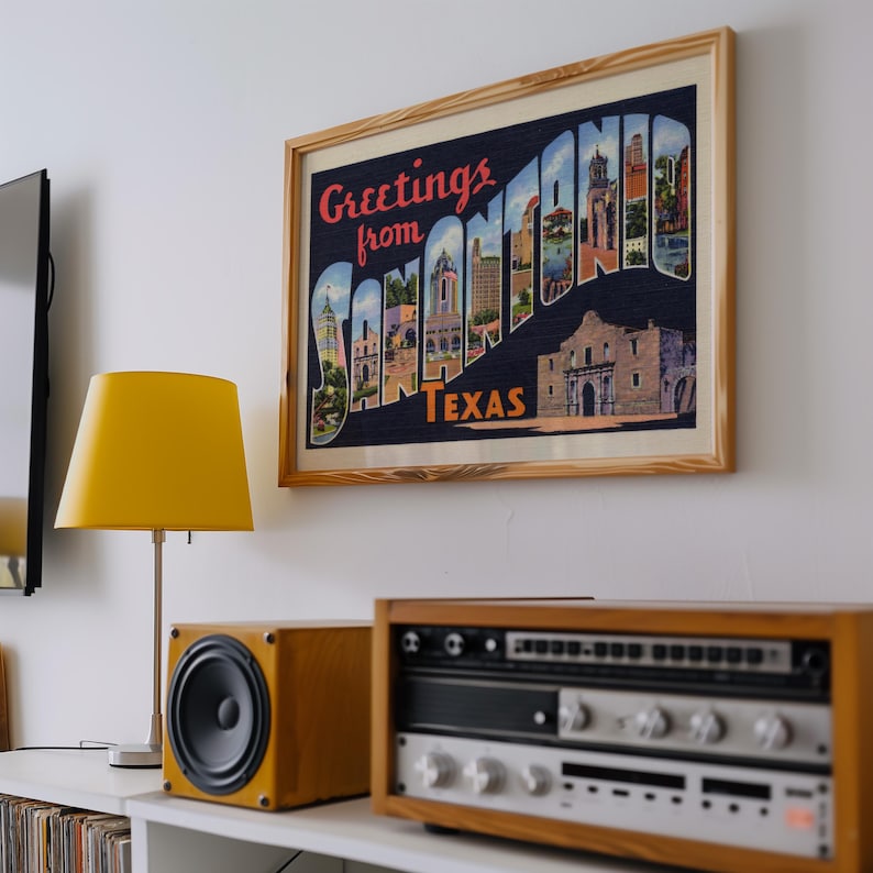 May include: A framed print with the words "Greetings from San Antonio Texas" in a vintage postcard style. The print is above a yellow lamp and stereo equipment.