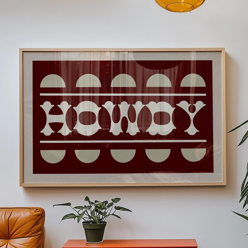 May include: A framed print with a burgundy background and white text that reads "HOWDY". The text is surrounded by a pattern of white semi-circles.