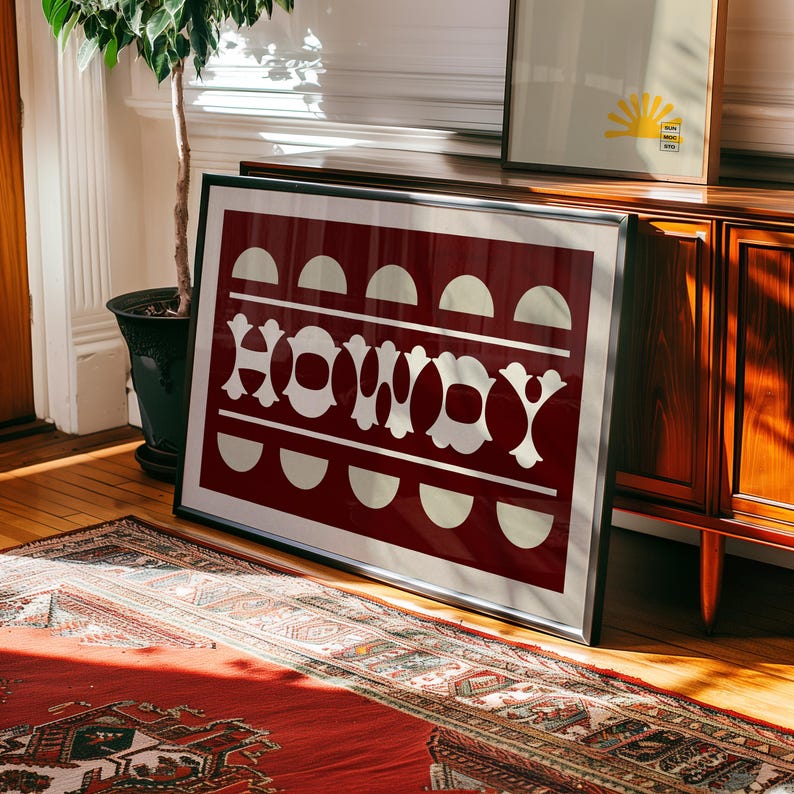 May include: A framed print with a red background and white text that reads "Howdy". The text is stylized with a geometric design. The print is framed in a black frame.