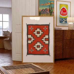 May include: A framed print of a red, white, and black geometric pattern rug. The rug has a traditional Native American design with crosses and squares.