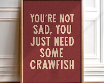 Op de afbeelding: Een ingelijst print met een rode achtergrond en witte tekst die "You're not sad, you just need some crawfish" zegt.